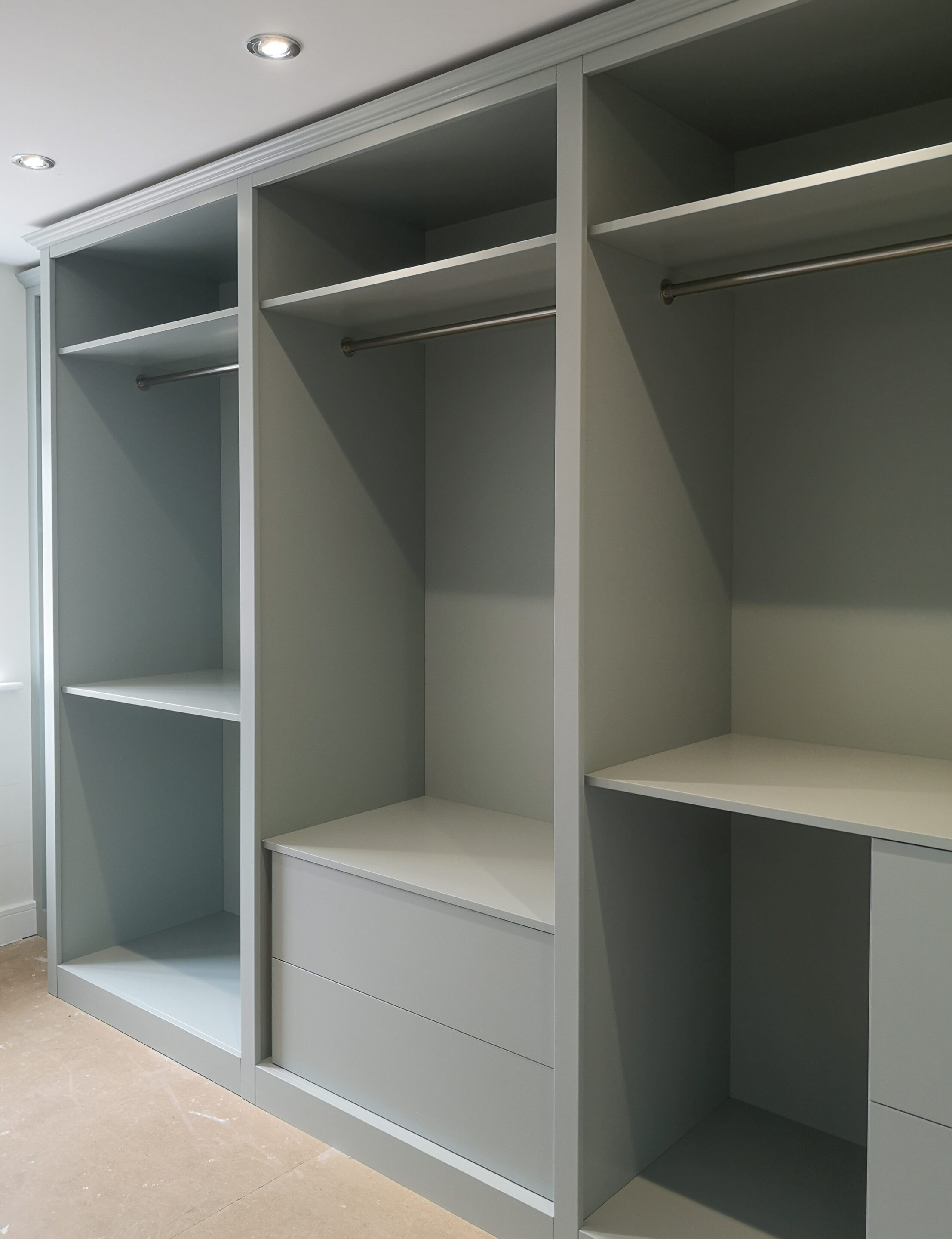 The picture shows the full length of the bespoke dressing room wardrobes, left open to showcase the clothing. Fitted with a combination of hanging rails at different lengths and drawers.