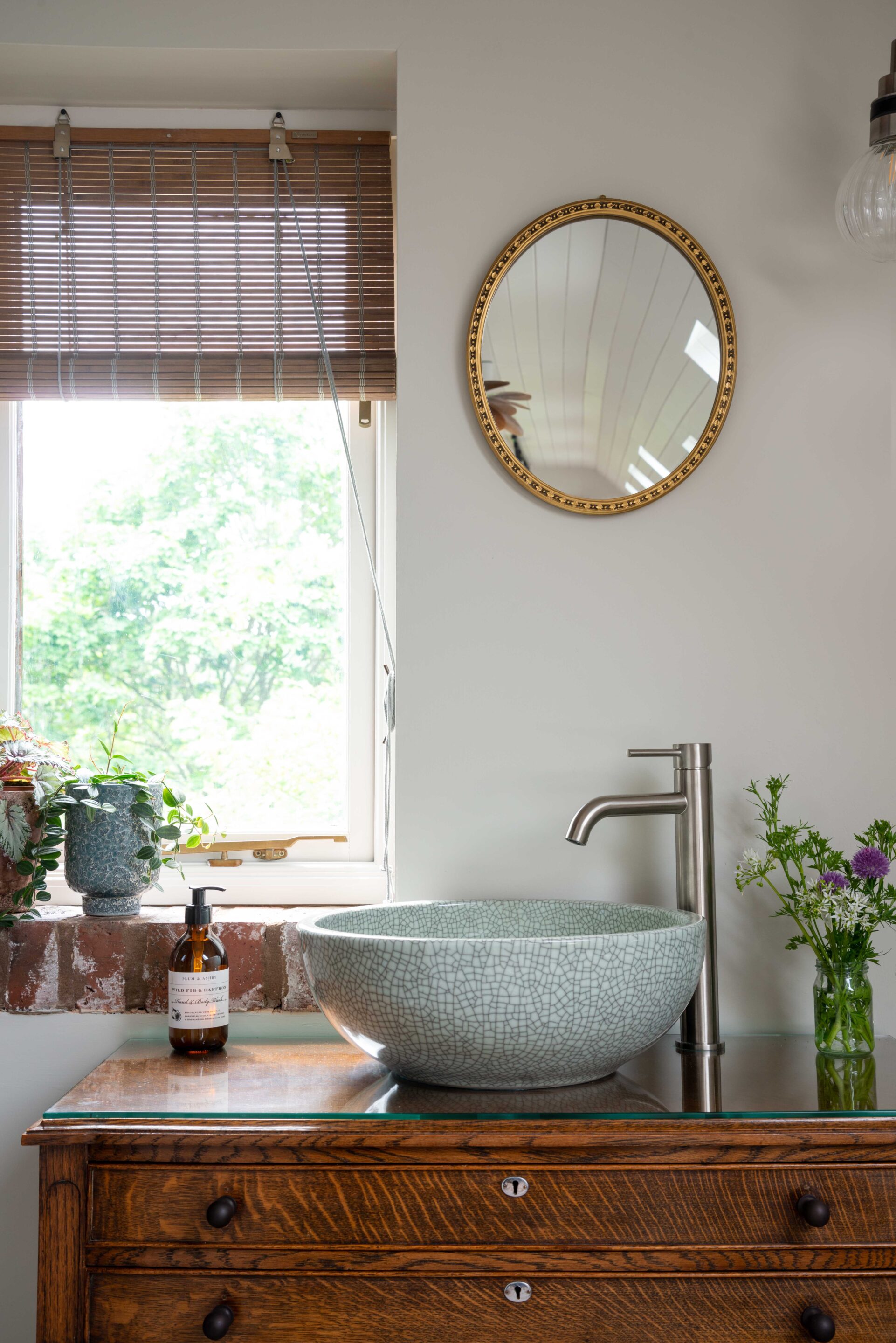 A close up of a vintage vanity unit with Nickel taps and round, green, crackle effect wash bowl