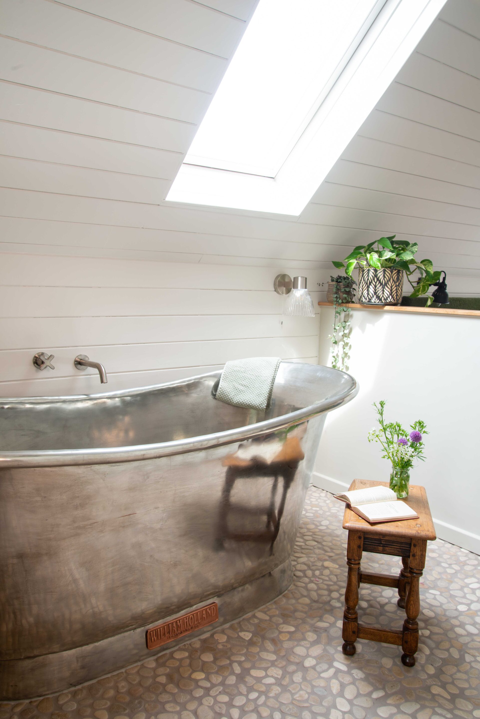 A freestanding copper Bateau bath, finished in tin, on top of pebble mosaic floor tiles