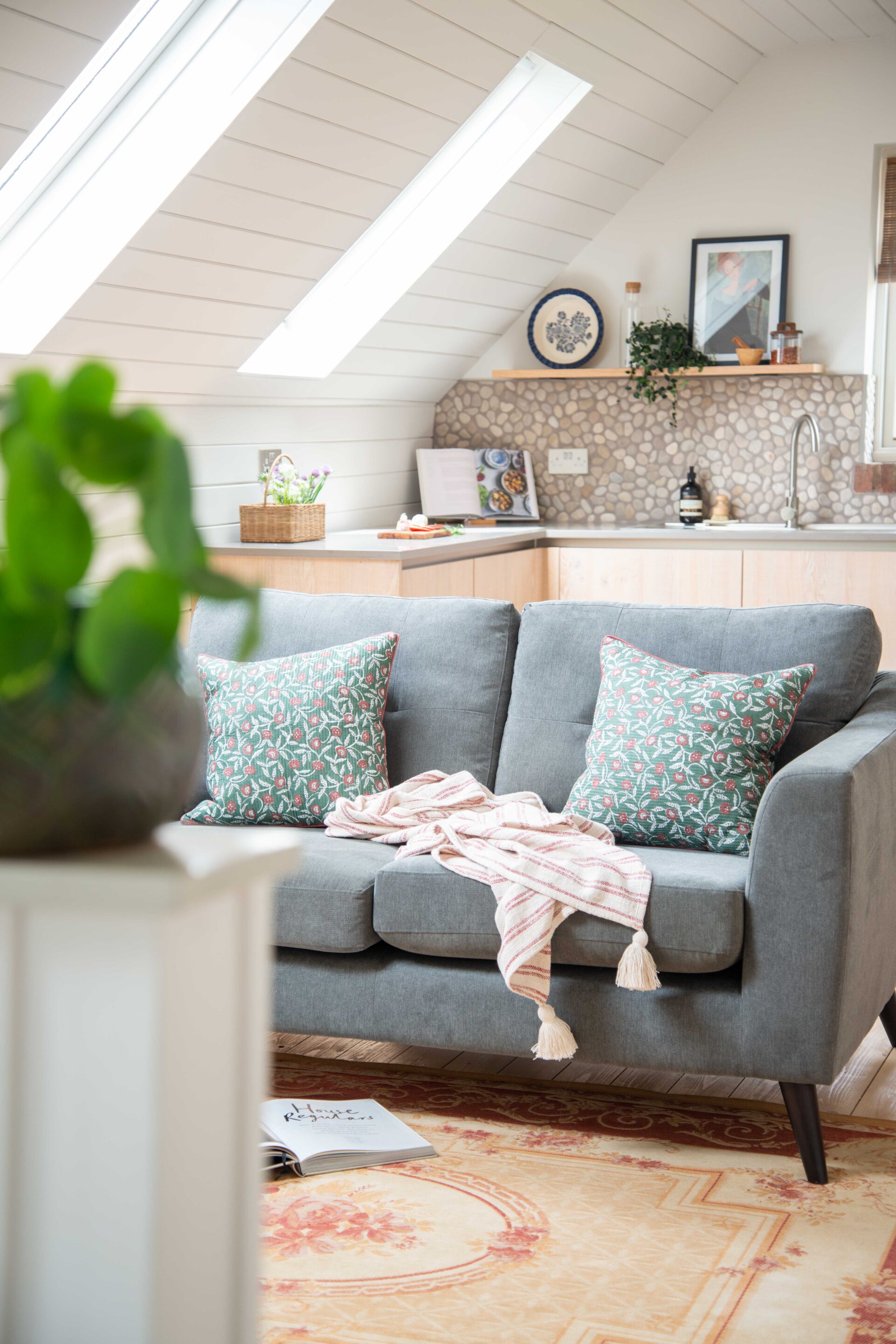 A view into the kitchen of a loft studio, across a small sofa with pink and green cushions.