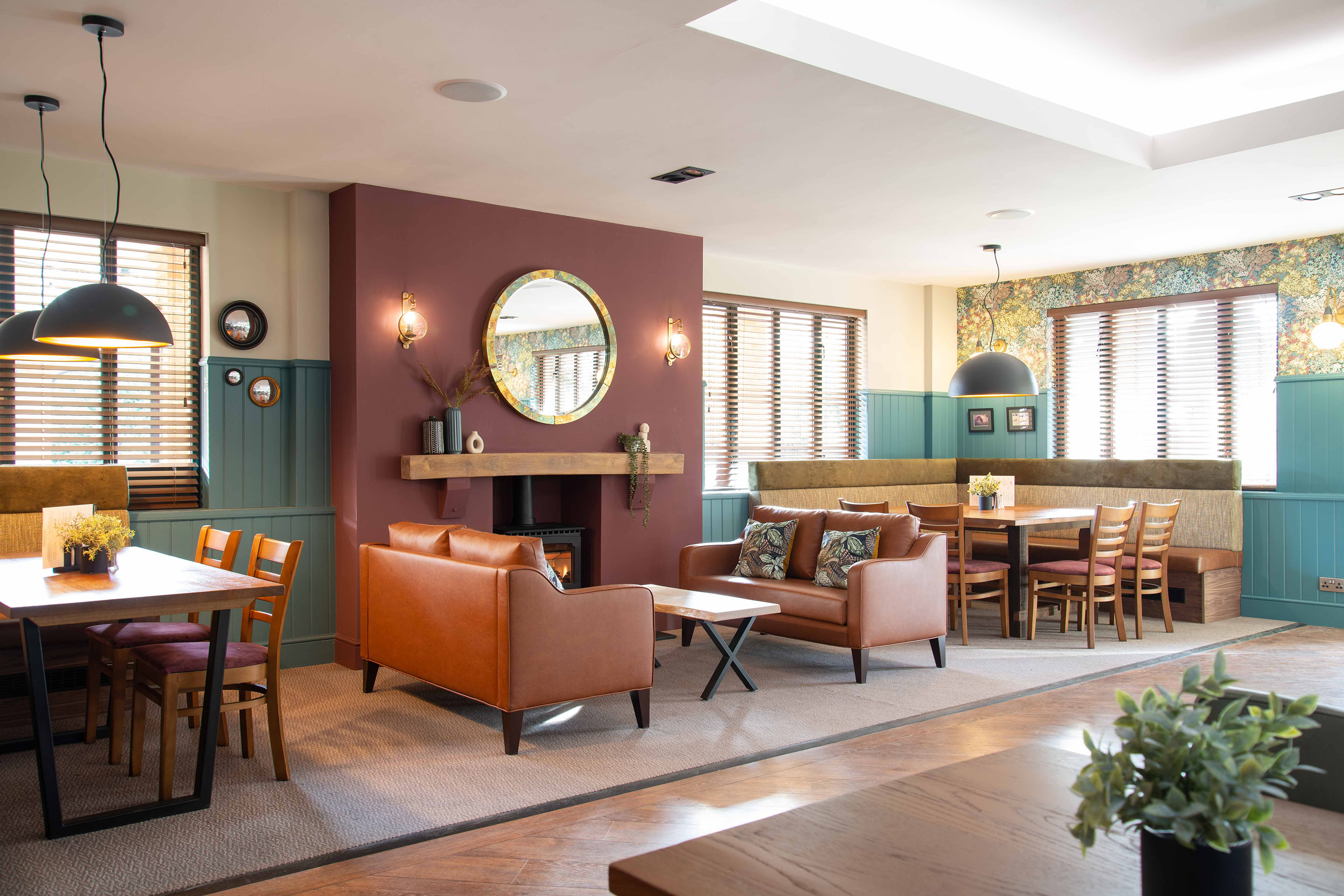 A full view of the fireside area with two sofas and two large tables for family dining. Pendants hang above the tables to create an intimate setting. Part of the Bar Restaurant Interior Design at Bromsgrove Golf Centre