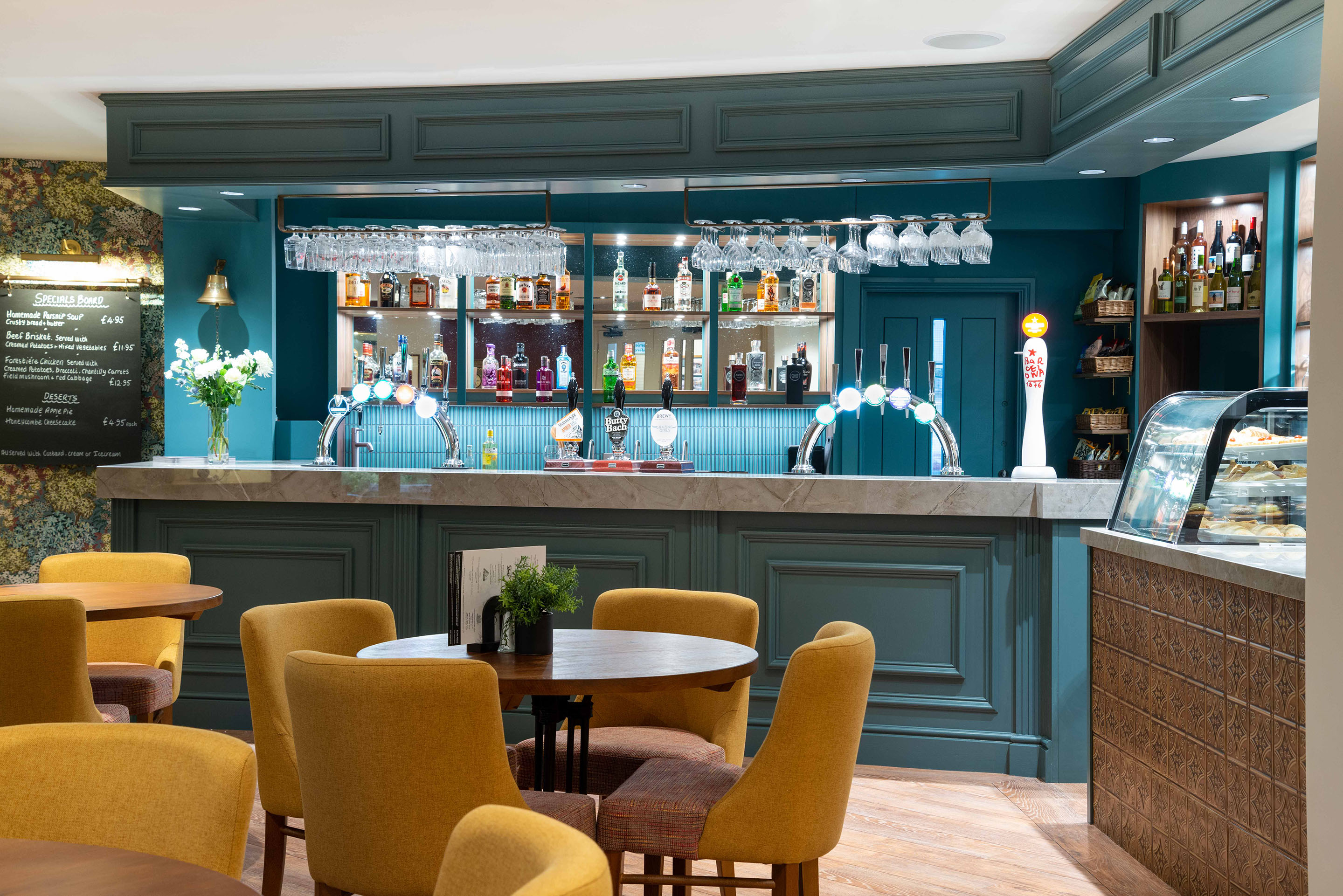 The brand new bar at Bromsgrove Golf Centre which has been sprayed in Dark Blue with a custom Dekton surface. Hanging rails suspend glassware above the bar and the lights from the new bespoke bar cabinetry shine behind. Part of the Bar Restaurant Interior Design at Bromsgrove Golf Centre