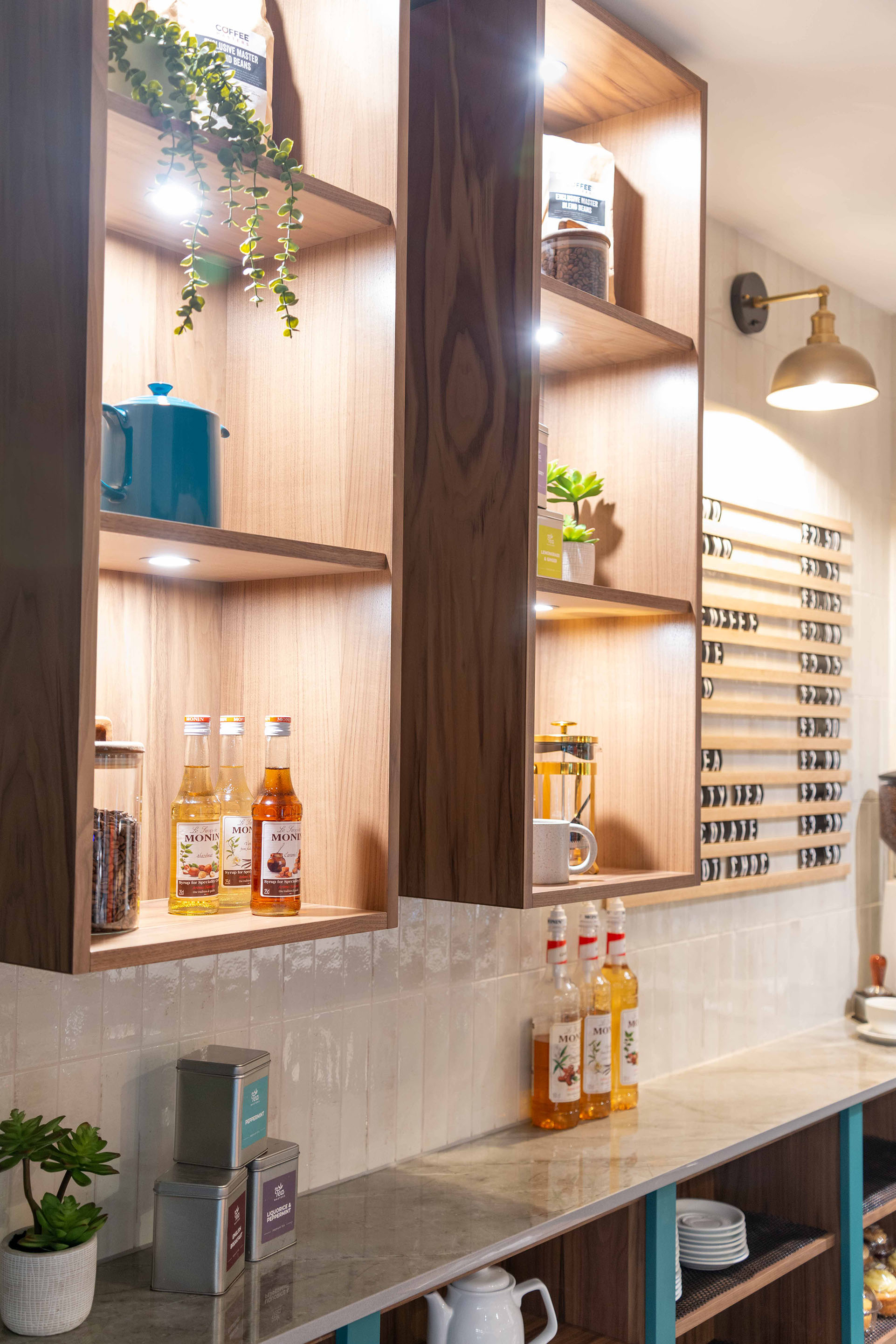 Bespoke shelving in Walnut Veneer displays teas, coffees and plants in the coffee bar. Part of the Bar Restaurant Interior Design at Bromsgrove Golf Centre