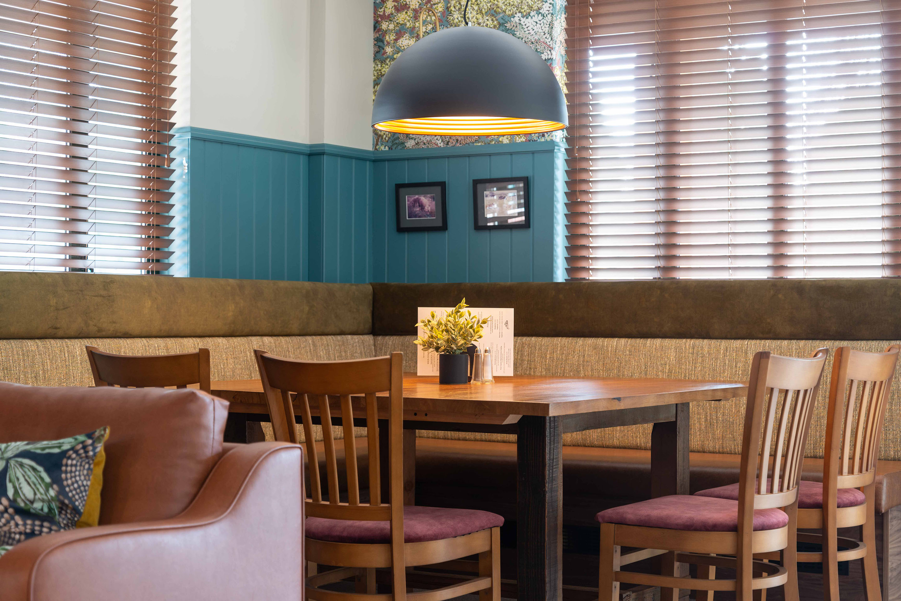 A large square corner table with banquette seating and wooden back chairs creates a cosy seating space for 8 people. Part of the Bar Restaurant Interior Design at Bromsgrove Golf Centre