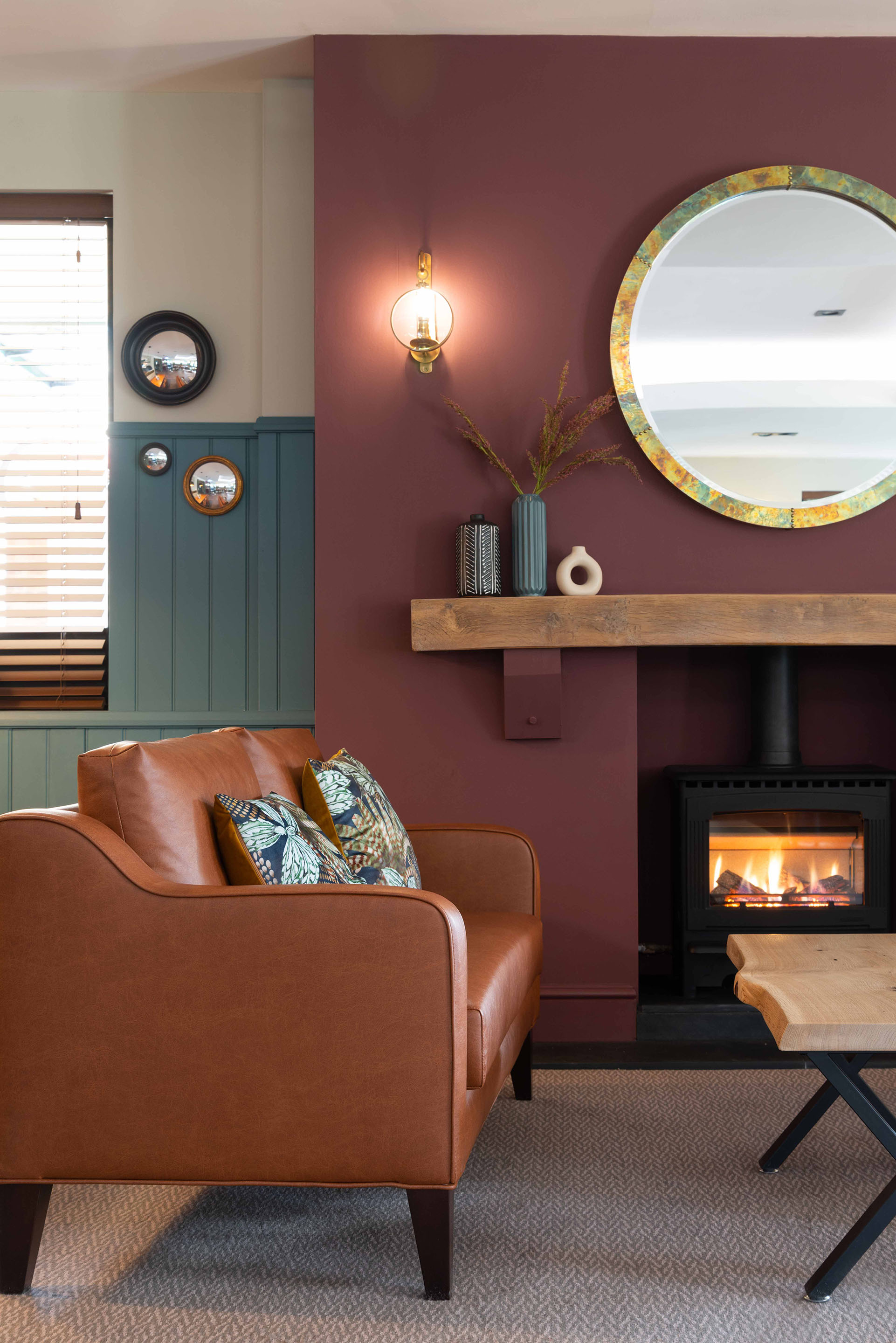 A cosy fireside setting with leather sofa against a deep red wall. Part of the Bar Restaurant Interior Design at Bromsgrove Golf Centre