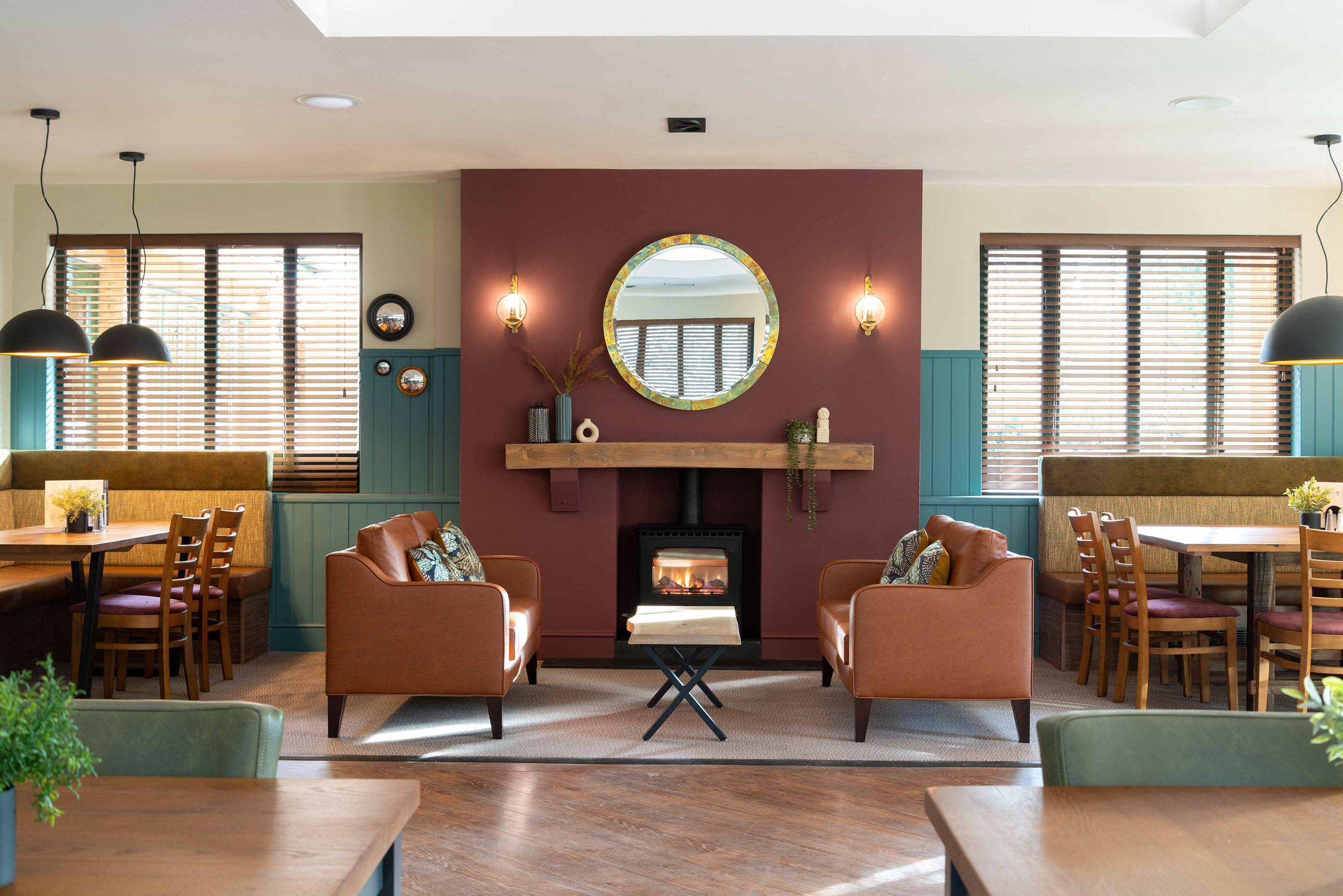 A full view of the fireside area with two sofas and two large tables for family dining. Pendants hang above the tables to create an intimate setting. Part of the Bar Restaurant Interior Design at Bromsgrove Golf Centre