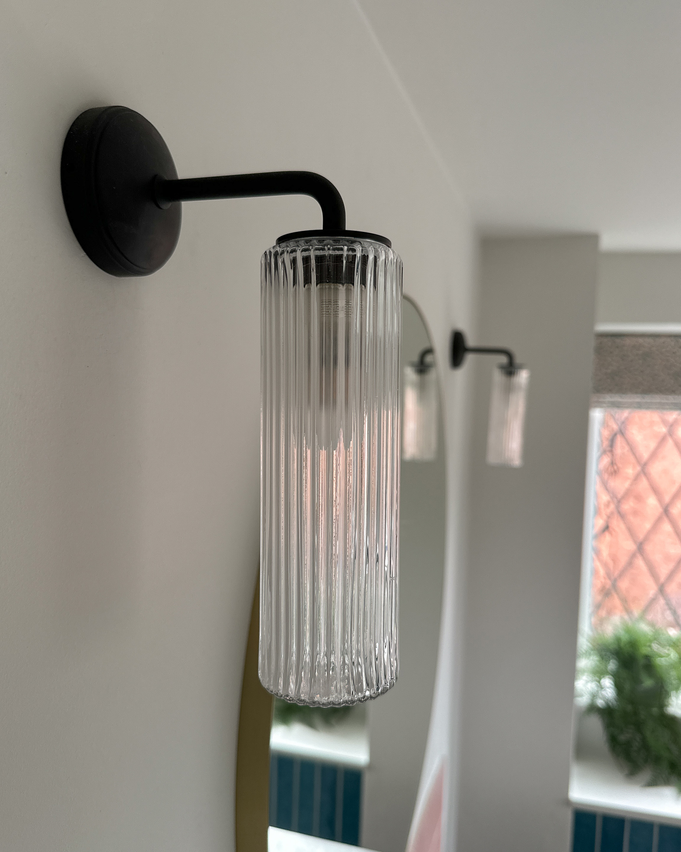Bathroom wall lights in bronze with fluted glass from Corston Architectural are situated either side of the round mirror.