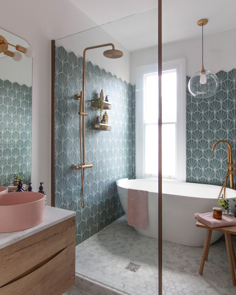 A snapshot of a wetroom area in a small victorian bathroom in Leamington Spa. Showing Hexagonal teal wall tiles, marble mosaic floor tiles, a brushed gold shower with rainfall head and a pink concrete basin. A Bathroom Pendant light hangs over the bath.