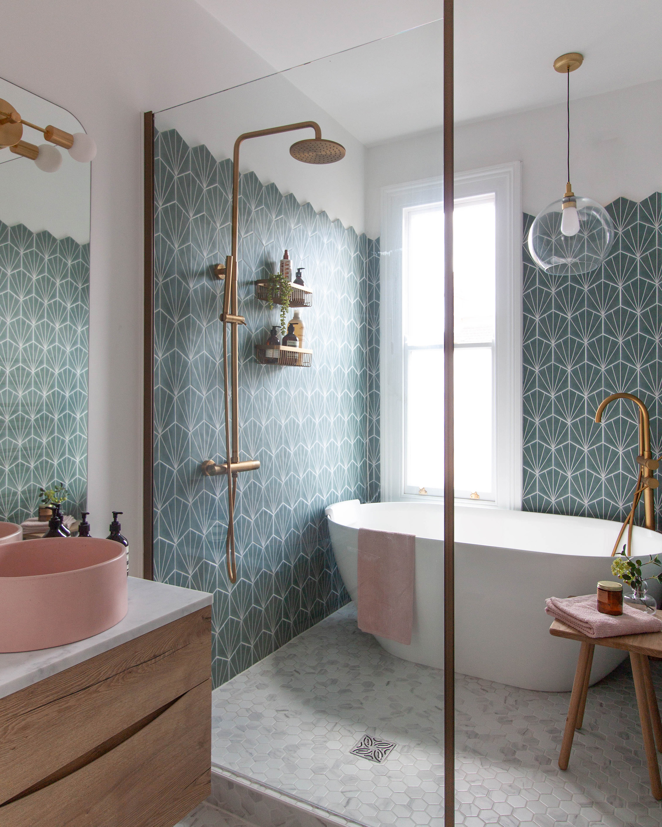 A snapshot of a wetroom area in a small victorian bathroom in Leamington Spa. Showing Hexagonal teal wall tiles, marble mosaic floor tiles, a brushed gold shower with rainfall head and a pink concrete basin. A Bathroom Pendant light hangs over the bath.