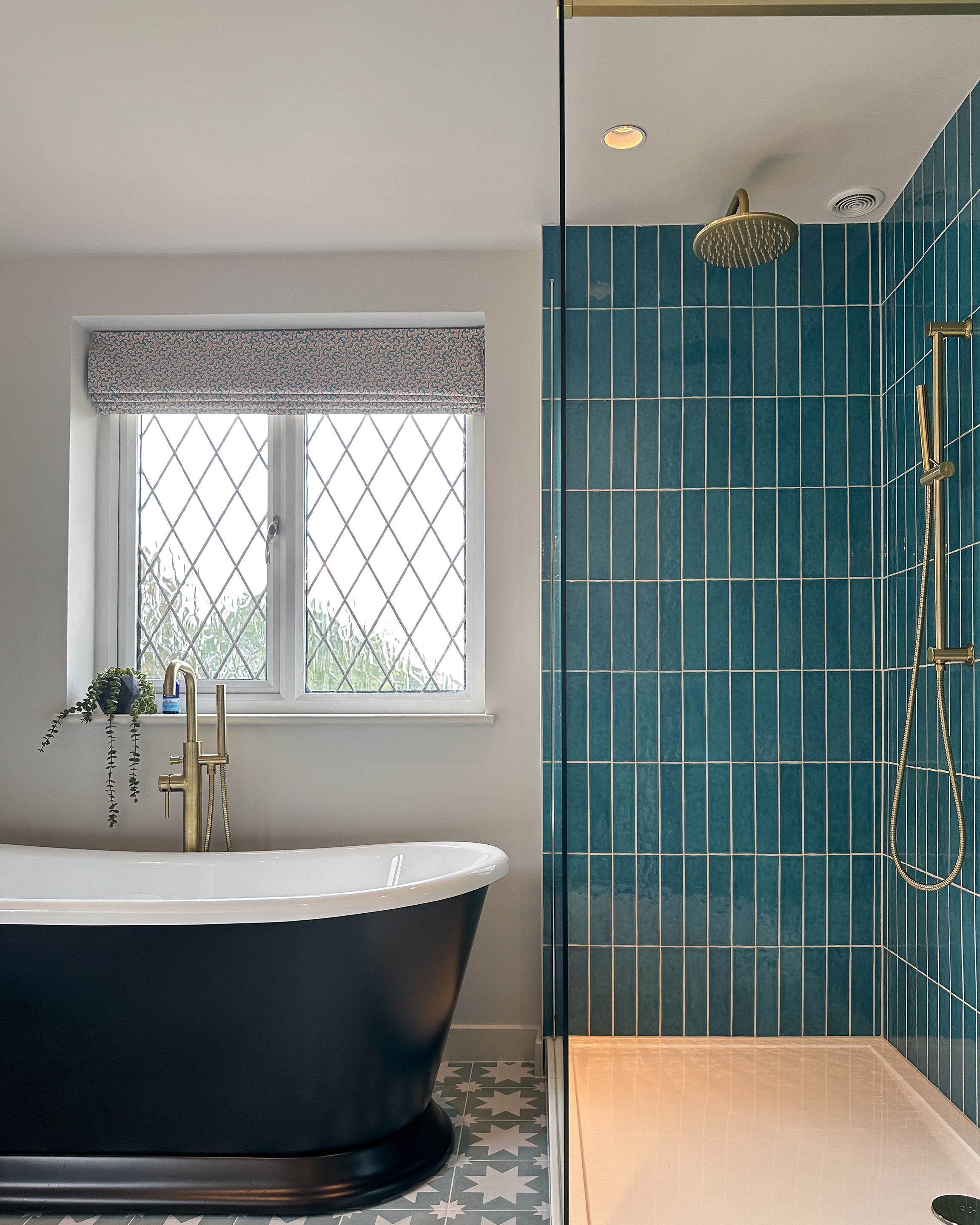 This picture shows a shower area with blue tiles laid in a vertical pattern, with brass rainfall shower head. You can also see the traditional style black roll-top bath.