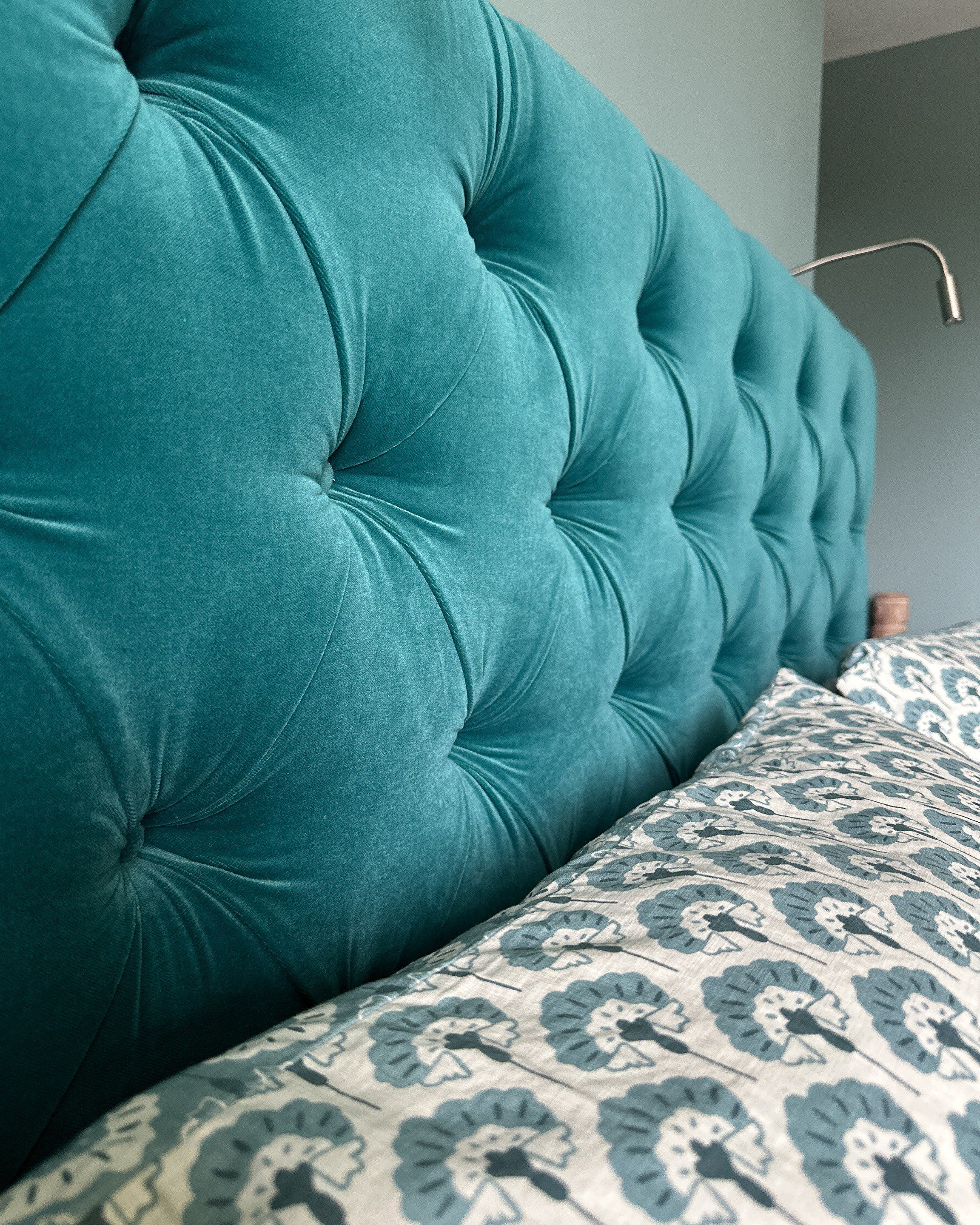 Close up of headboard which is teal velvet linen, with a teal motif pillow.