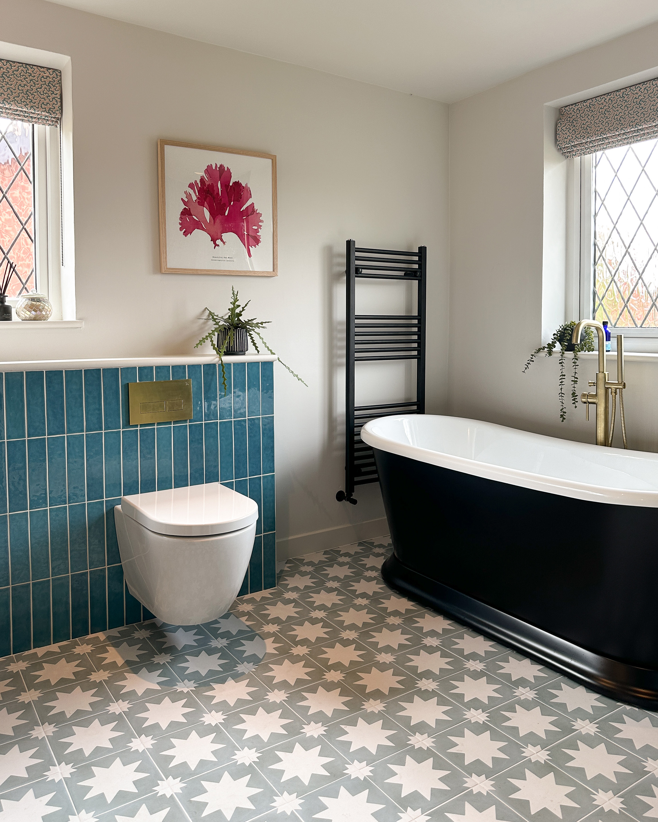 This picture shows a bathroom with a new floating loo against blue tiles. The floor tiles have a bold star pattern, and the bath is a traditional style roll-top bath in black.