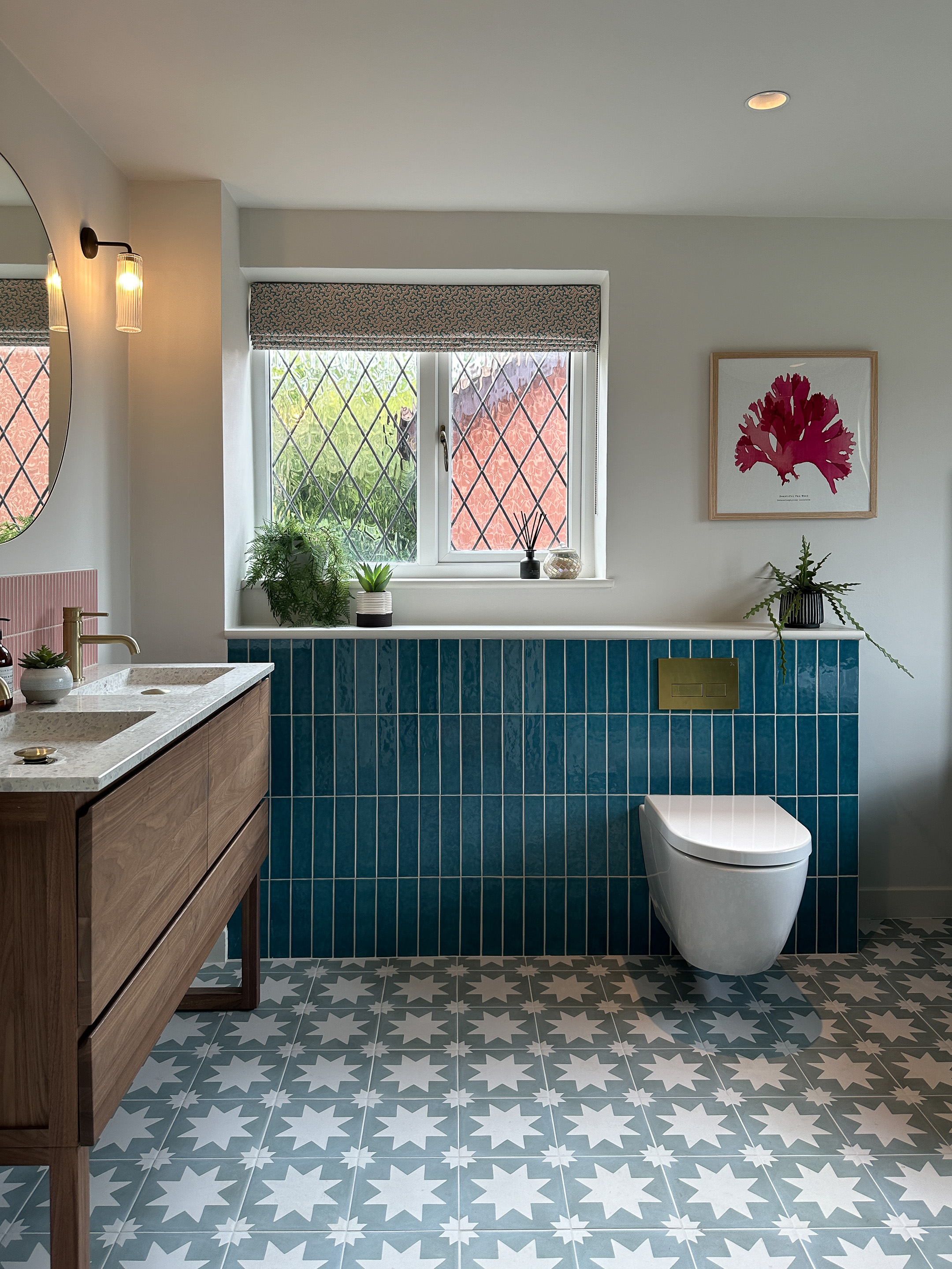 This picture shows a bathroom with a new floating loo against blue tiles. The floor tiles have a bold star pattern, and the vanity unit is walnut with a terrazzo top.