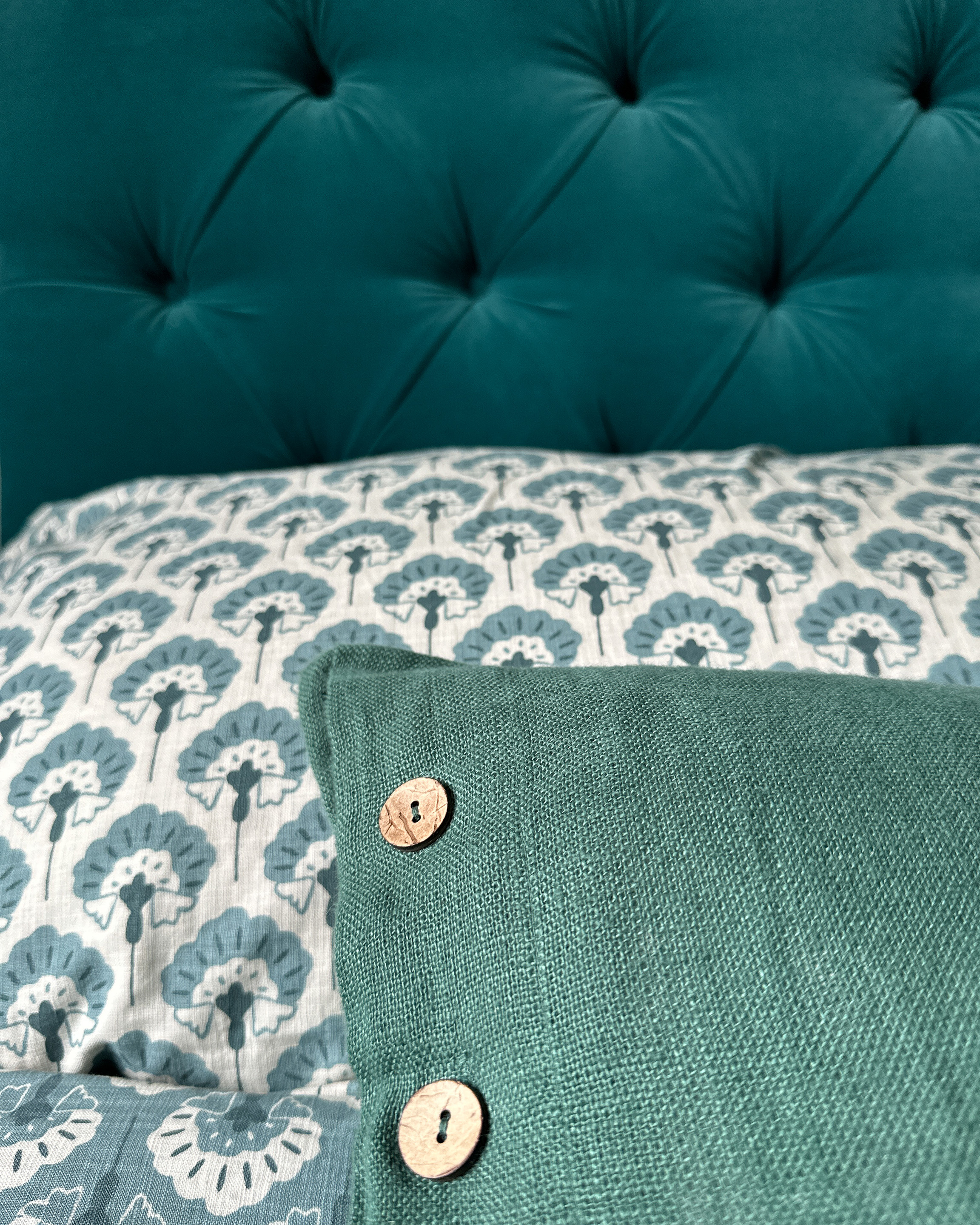 Close up of headboard which is teal velvet linen, with a teal motif pillow and a complementary cushion.