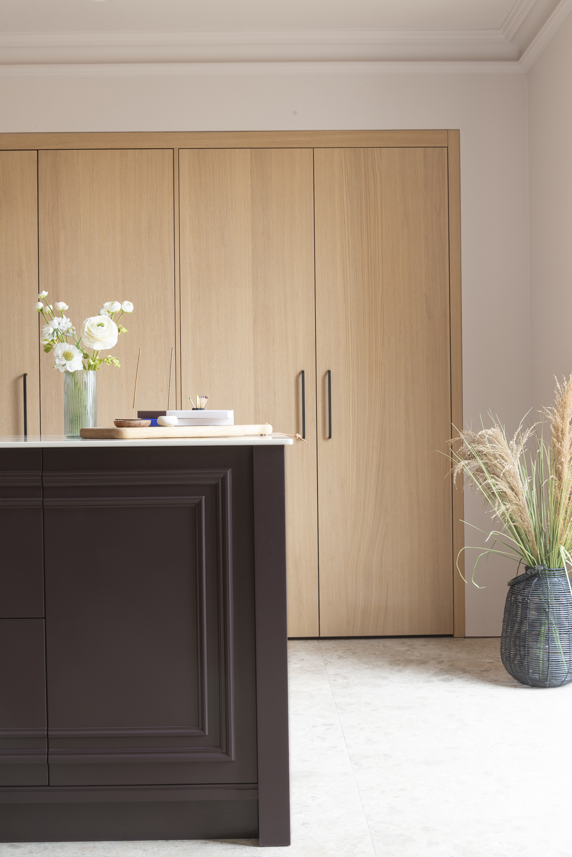 A bespoke kitchen, showing a traditional style kitchen island, with contemporary floor to ceiling oak cabinetry and stone coloured terrazzo flooring.