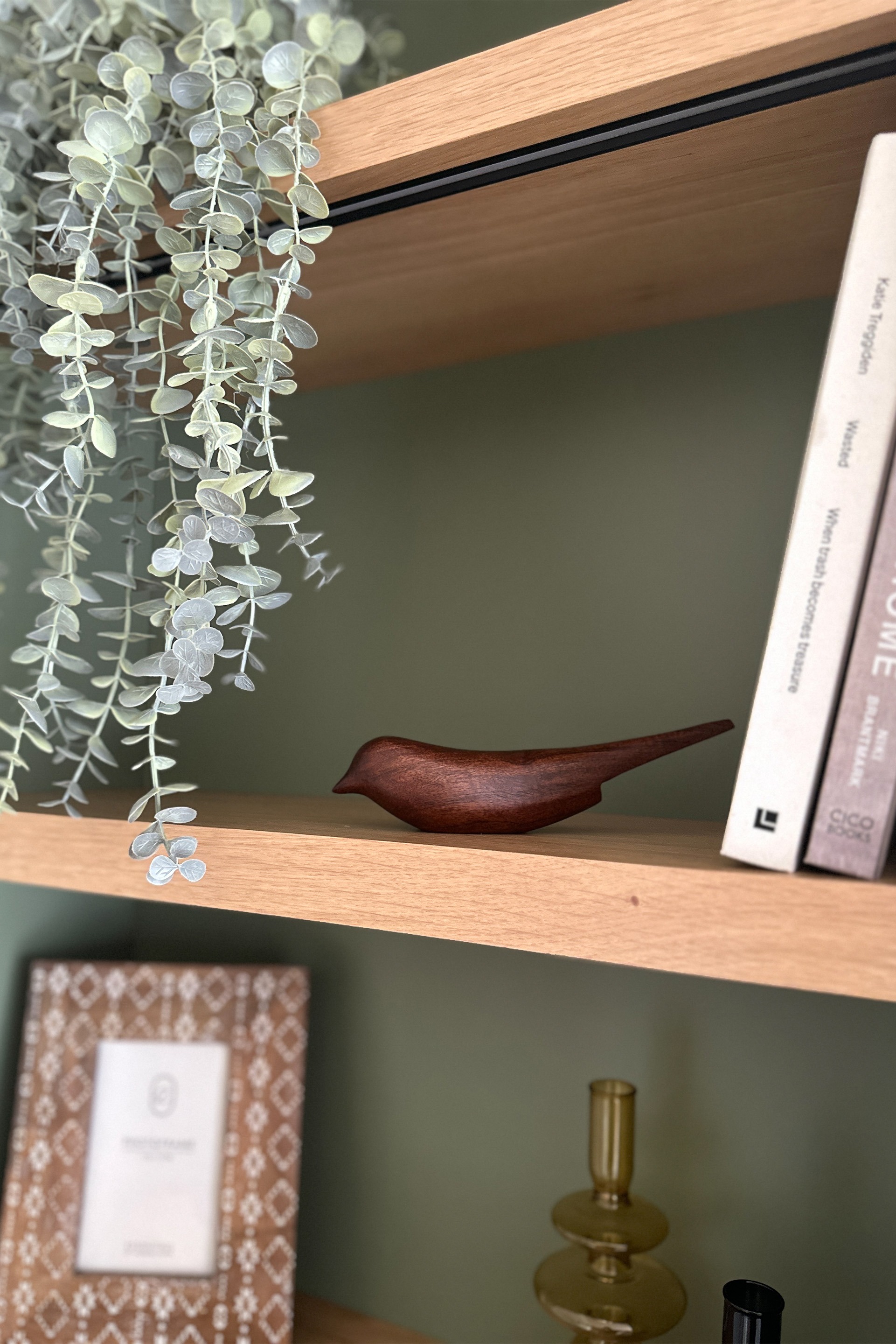 detail of the bespoke bookcase with oak veneer shelves and integrated lighting. a wooden bird ornament is sitting on the shelf with plants and books