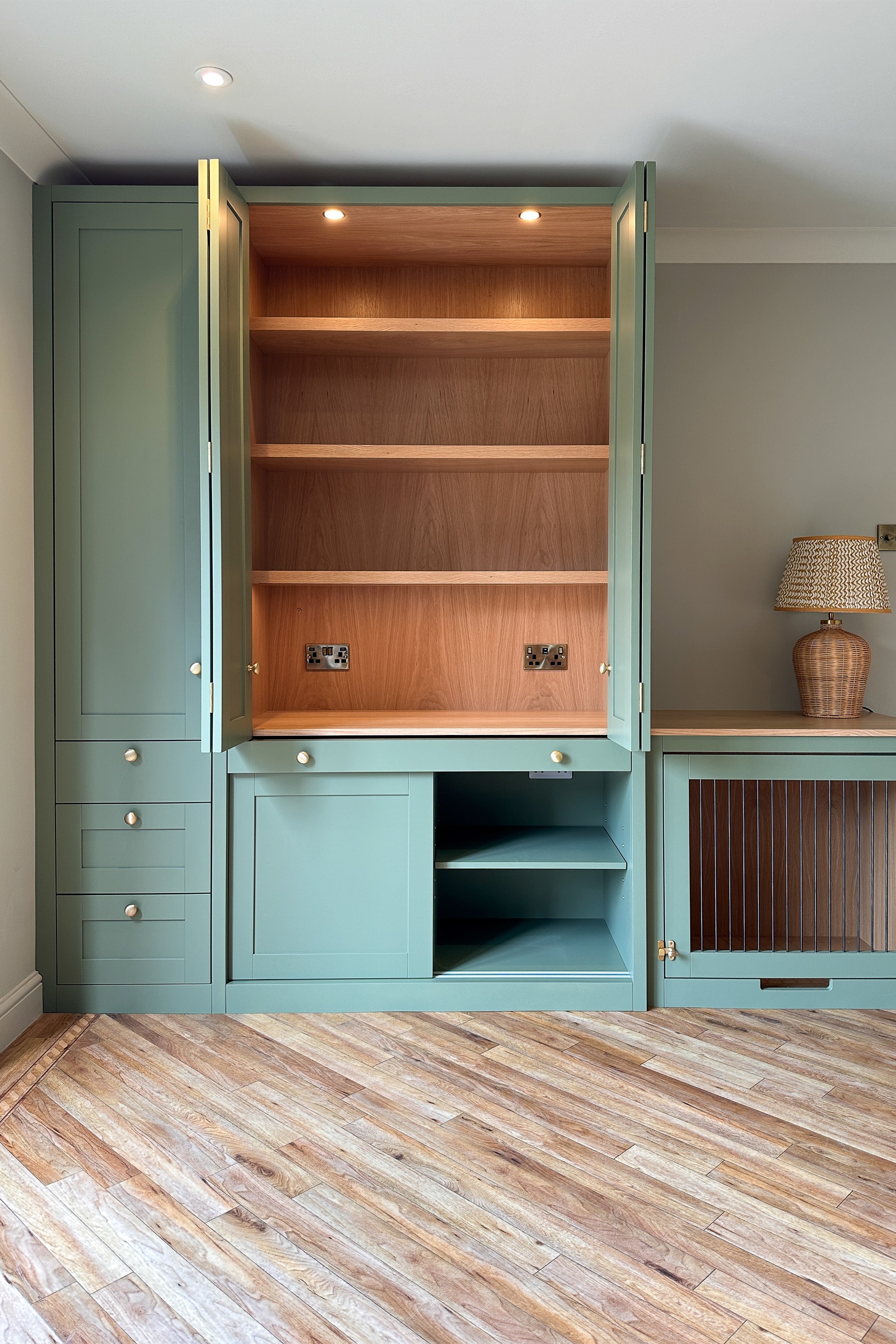 a bespoke home office featuring a wide desk space with bi-fold doors and pull out shelf for laptop, sliding doors underneath and cabinetry to either side