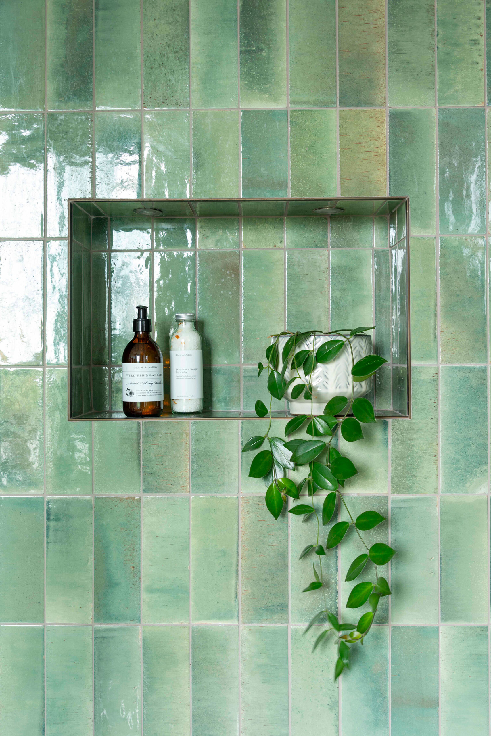 Niche shelving in the shower, with rustic green glazed tiles and bronze trim finish.