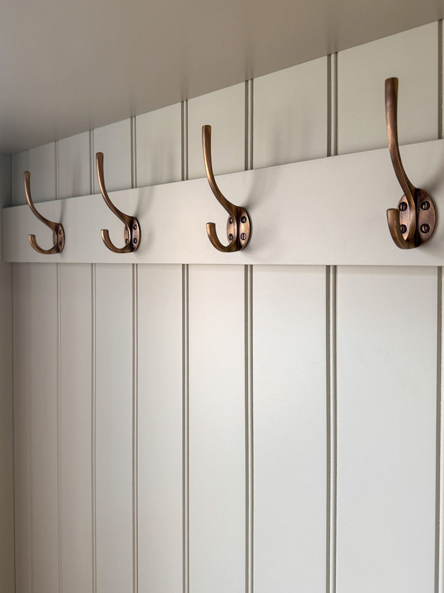 The image shows the traditional brass coat hooks that form part of a bespoke boot room hanging space from No.54 Interiors