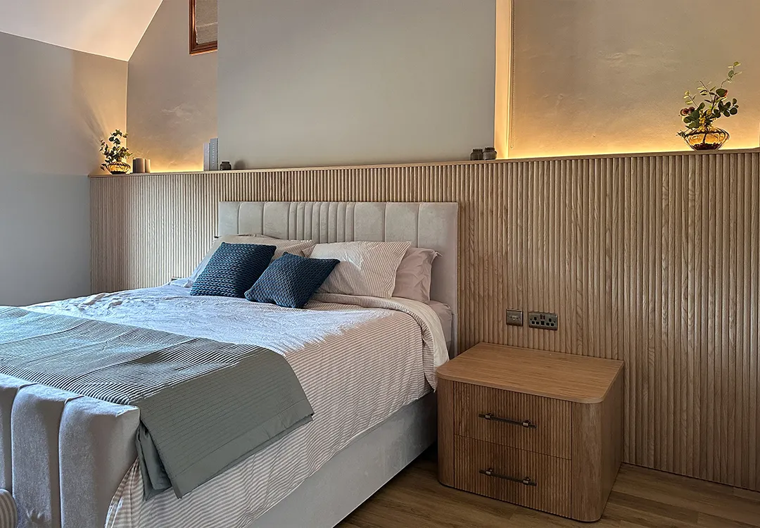 Bespoke bedroom with wall-to-wall reeded oak panelling, integrated alcove lighting and a curved oak bedside cabinet.