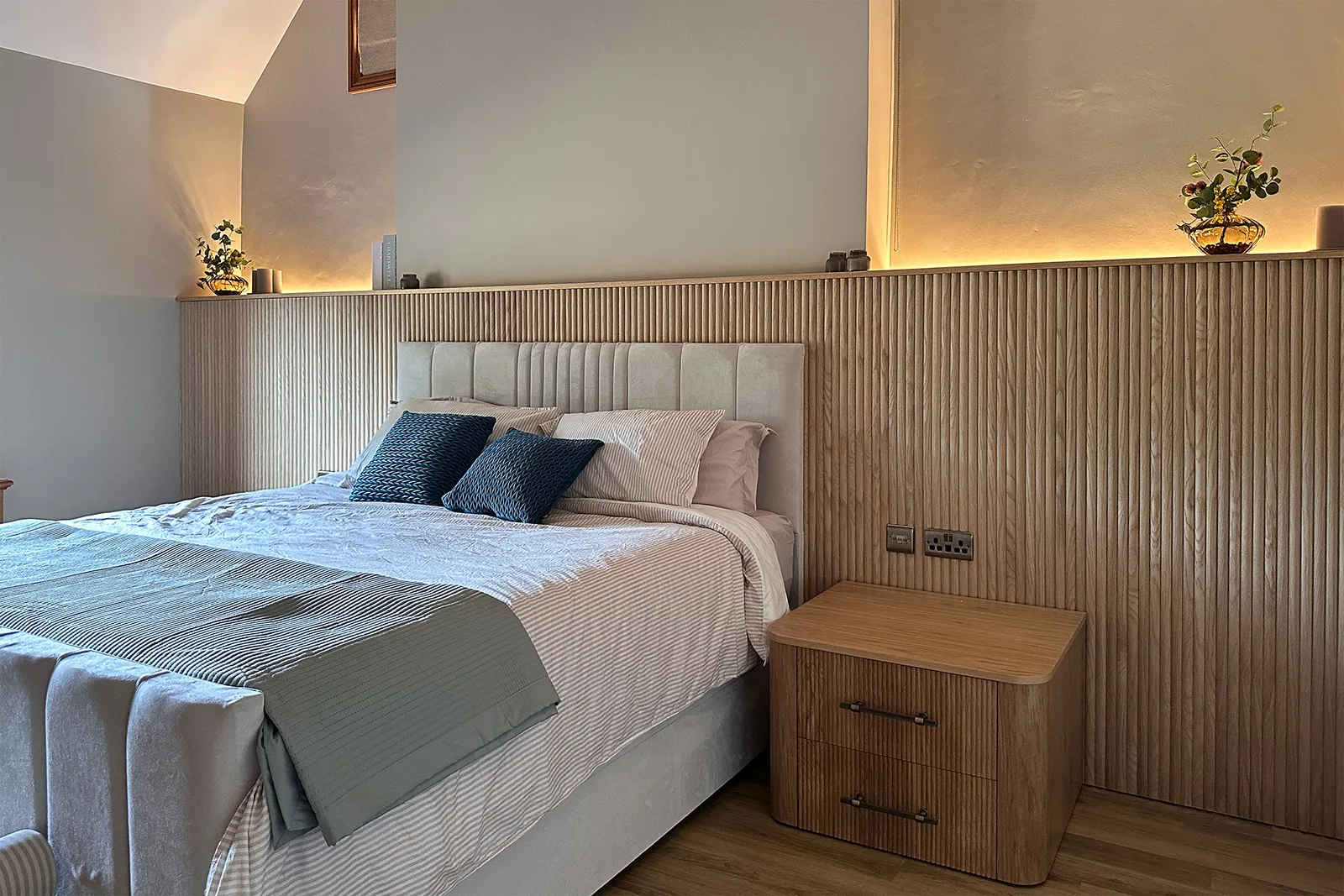 Vaulted bedroom with full-width reeded oak panelling and bespoke curved bedside table