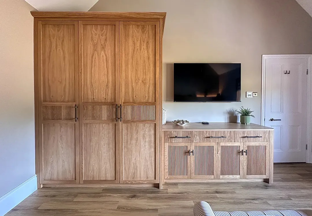 Triple oak wardrobe with reeded Shaker doors and a coordinating four-door dresser positioned beneath a wall-mounted television.