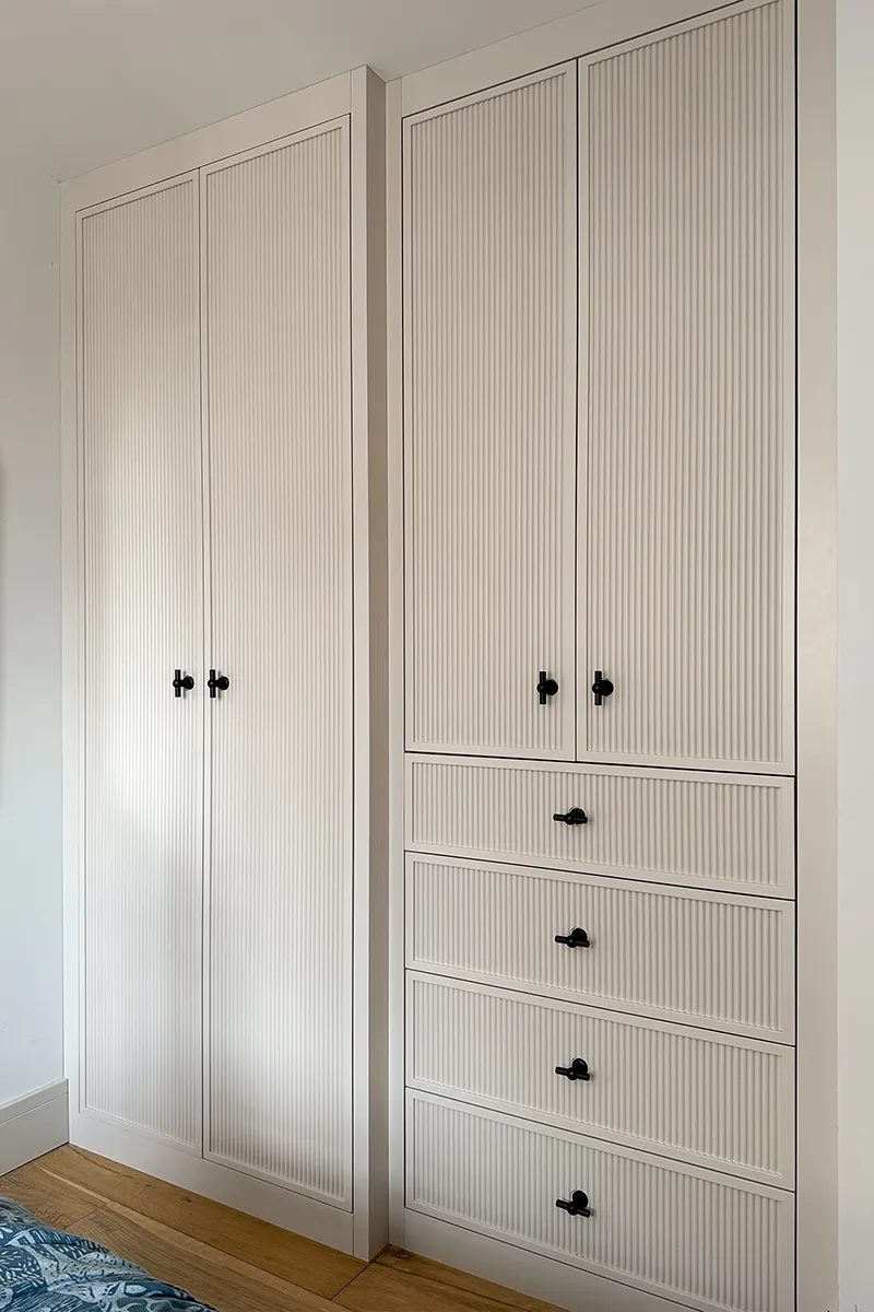 Bespoke fitted wardrobes with reeded painted doors, integrated doors and contrasting bronze handles.