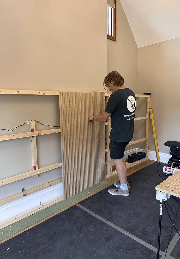 Shaun fitting a section of reeded oak panelling to the timber framework behind a bespoke bedroom headboard feature.