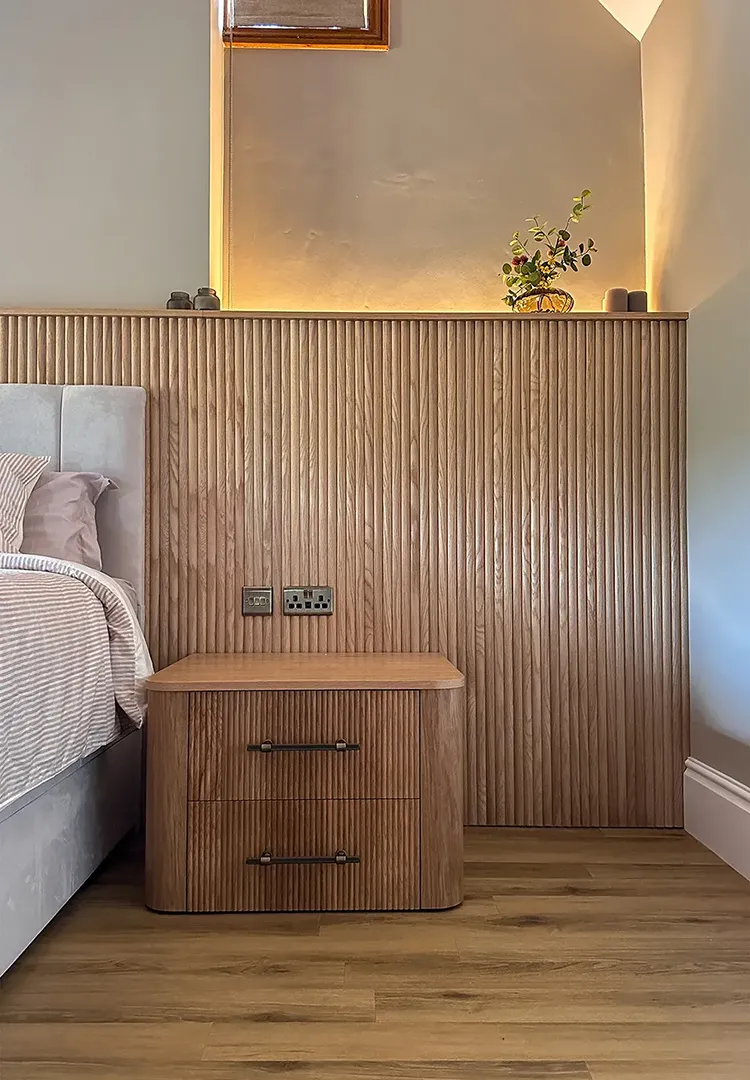 Close-up of bespoke reeded oak wall panelling with a continuous oak shelf and concealed warm LED lighting within the bedroom alcove.