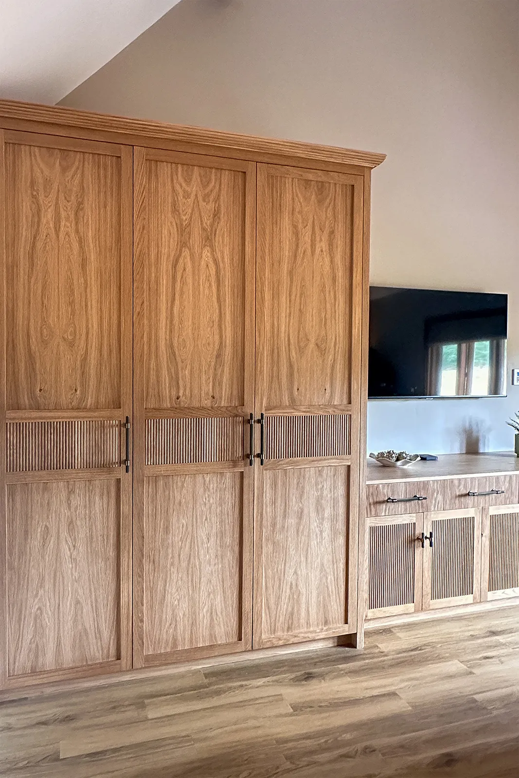 Bespoke oak wardrobe and matching low dresser with reeded doors in a vaulted bedroom