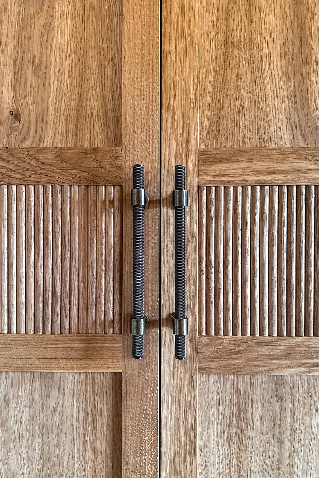 Close-up of reeded oak wardrobe doors with dark textured handles and bronze detailing