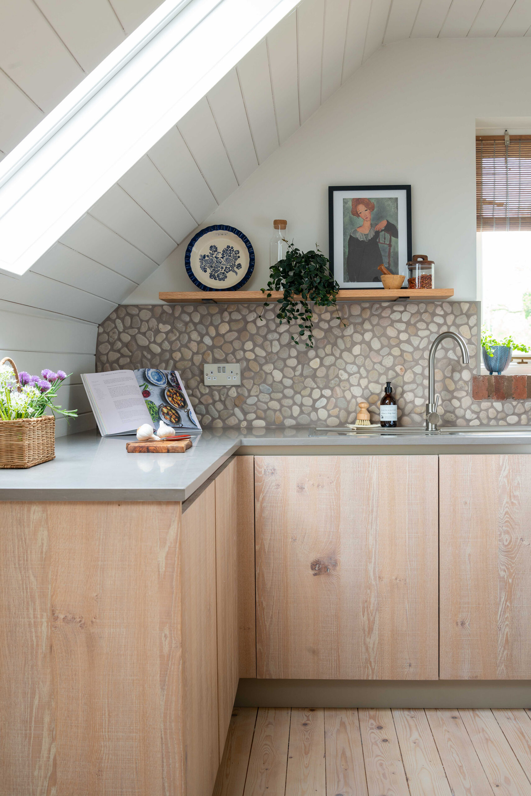 Oak fitted kitchen with integrated oven and patterned splashback beneath a sloping loft ceiling.