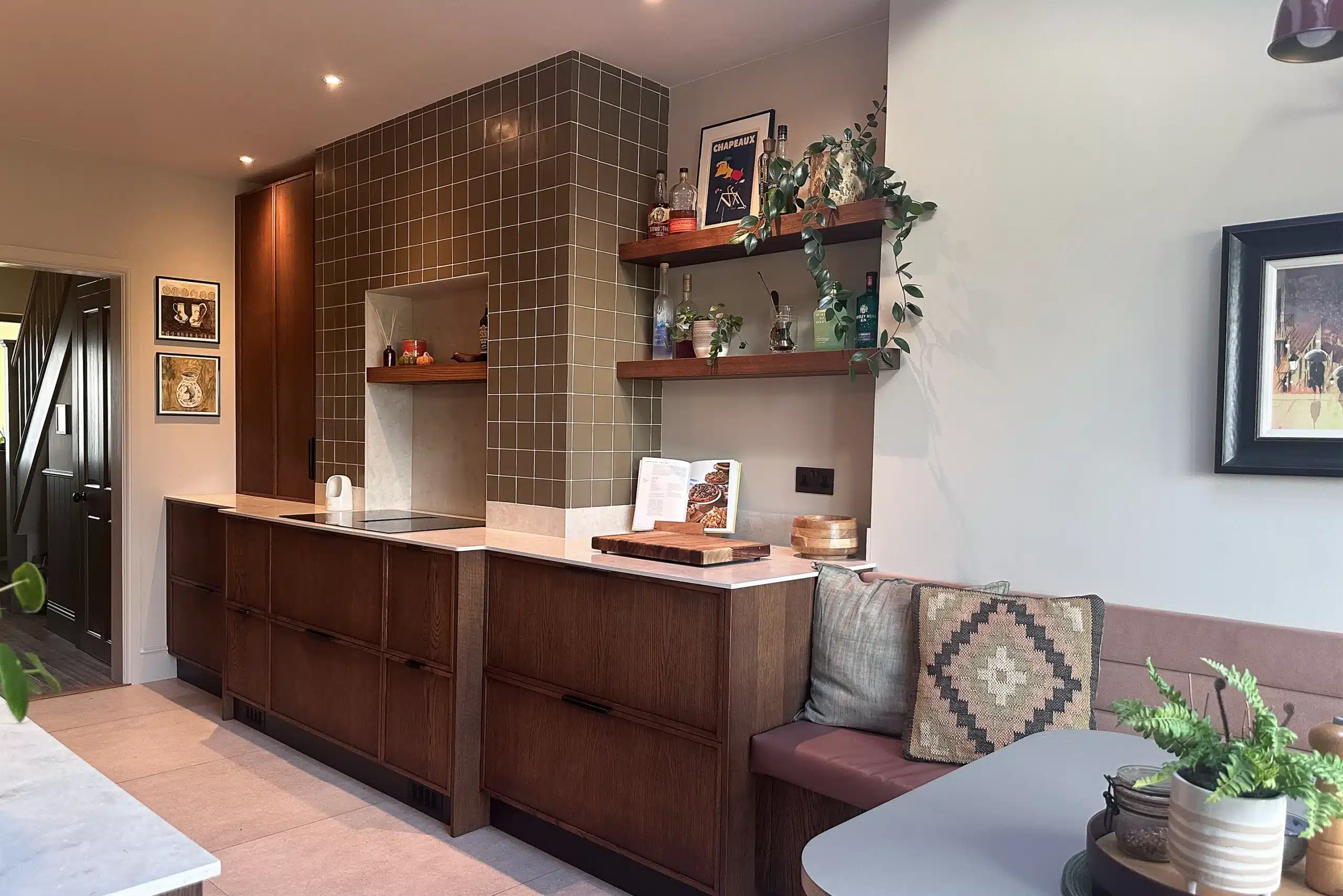 Dark oak kitchen cabinetry with a tiled cooking area, open timber shelving and built-in upholstered dining seating.