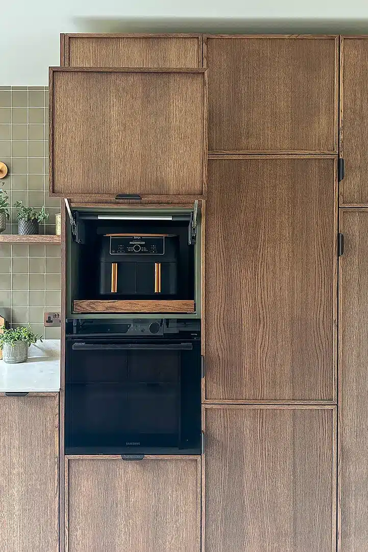 Custom oak kitchen cabinetry with an open lift-up cupboard housing an air fryer above an integrated black oven.